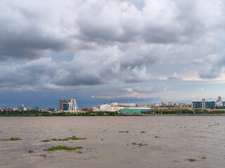 Naklejka premium View of the Malecon del Rio waterfront in Barranquilla, Colombia, with urban skyline, river landscape and dramatic cloudy sky, highlighting modern development along the Magdalena River.