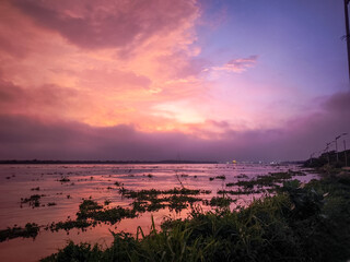 Warm sunset sky reflecting over the Magdalena River at Puerto Mocho, Barranquilla. Floating vegetation, calm waters and distant port lights create a natural and atmospheric river landscape in northern
