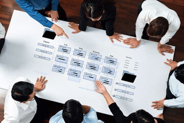 Business professionals collaborate over a large table, analyzing a detailed flowchart and data...