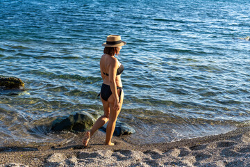 Woman, beach, sea. Woman walking on a pebble beach, stepping into the clear blue sea, enjoying summer vacation
