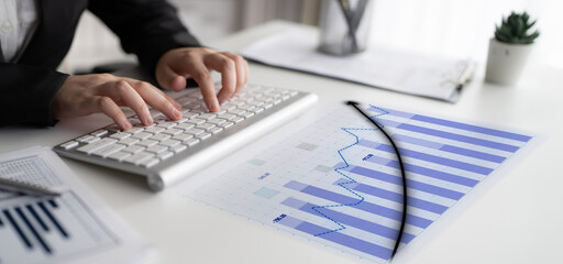 A professional analyzes financial data on a contemporary desk, focusing on stock market trends using a keyboard, charts, and documents in an office environment. Impute