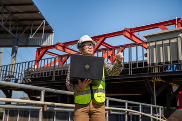 Naklejka premium Professional engineer using laptop to inspect hydraulic infrastructure operations at industrial worksite