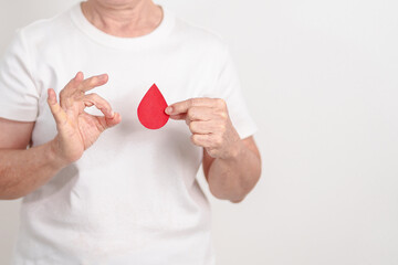 Elderly woman with red Blood drop paper for concept of June World Blood Donor day, Donation, January Blood donor awareness month, April Hemophilia awareness day, May Thalassemia Day, Anemia awareness