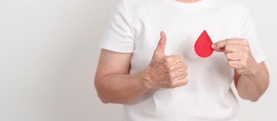 Elderly woman with red Blood drop paper for concept of June World Blood Donor day, Donation, January Blood donor awareness month, April Hemophilia awareness day, May Thalassemia Day, Anemia awareness
