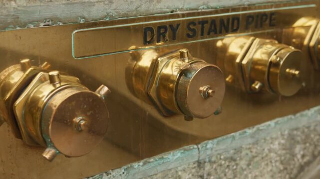 Dry standpipe compliance inspection closeup with polished caps, safety auditor checks fittings against regulation, embossed markings and concrete surround, maintenance window in built, fire safety