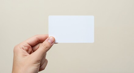 Fototapeta premium Hand Holding Blank Card: A close-up view captures a hand holding a clean, blank card, perfect for showcasing information or design, with neutral background