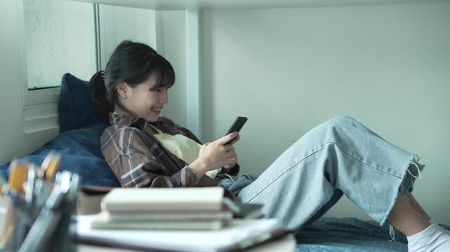 Asian girl lying on bunk bed using smartphone chatting