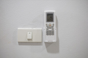 The light switch and remote control for the air conditioner are mounted on a white wall.