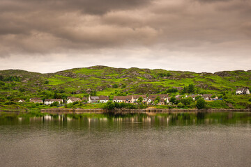 2023-06-07 THE TOWN OF LOCHINVER IN LAIRG SCOTLAND WITH A LUSH HILL BEHIND AND A NICE REFLECTION IN THE WATER WITH AND A CLOUDY SKY