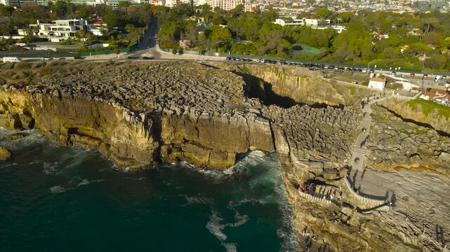 Aerial drone video orbiting around a famous tourist attraction called devils mouth or Boca do Inferno in Portugal coastline in Cascais during a sunny day, with turquoise waves hitting the tall cliffs.