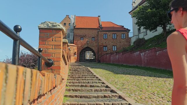 Elegant woman walking historic brick steps toward Grudziadz medieval gate