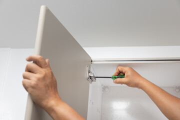 Close-up of a person adjusting a concealed hinge on a kitchen cupboard door.
