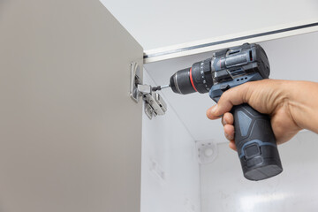 Close-up of a person adjusting a concealed hinge on a kitchen cupboard door.