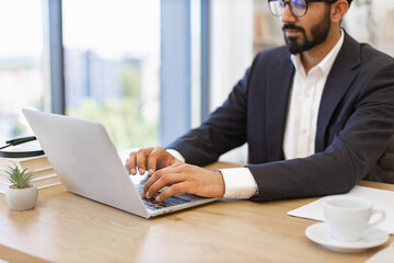 An Arab businessman is working on his laptop in a modern office setting