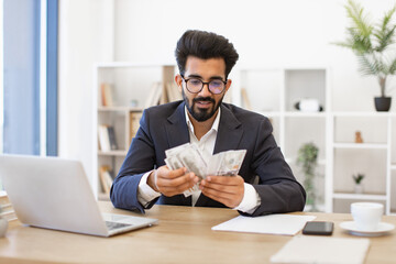 Obraz premium An Indian businessman in a suit counts a wad of cash at his desk, possibly after a successful deal
