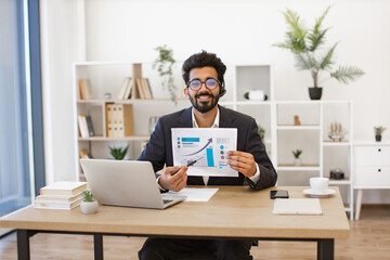 An Indian businessman is presenting financial data during a video conference, smiling and looking at the camera
