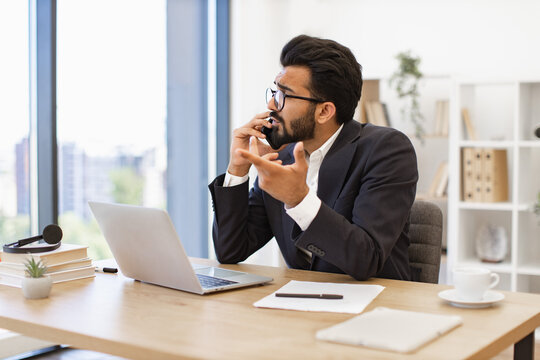 A man in a suit is on a phone call at his desk, looking concerned