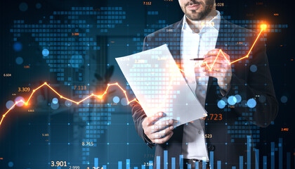 Businessman analyzing financial paper with glowing graph overlay on digital world map background in modern financial market concept scene.
