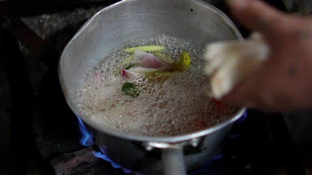4K pot of traditional Thai herbs including shallots lemongrass kaffir lime leaves galangal and carrots boils over open flame preparation of flavorful soup base.