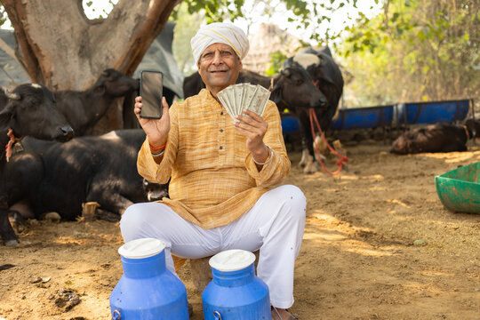 Happy Rural indian dairy farmer holding money and smart phone, earning and profits, Cattle Farming industry, Successful cow milk business. India economy. Wireless technology. Digital india.