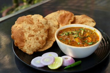 Puri sabzi on black plate with onion on the side