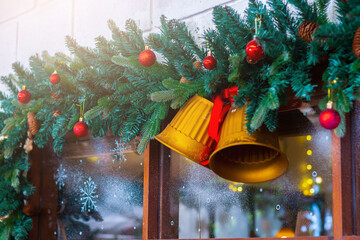 Festive Christmas decoration with evergreen garland, golden bells, and red ornaments hanging above a window, creating a warm holiday atmosphere.