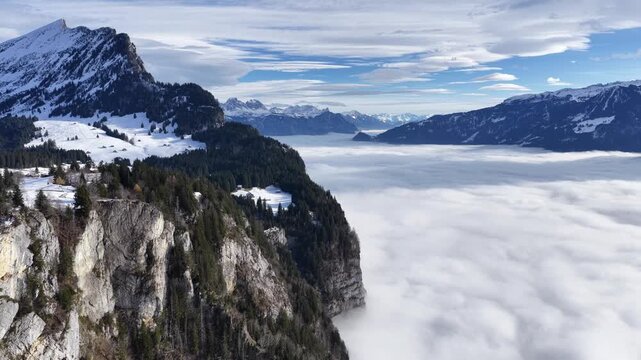 aerial - towering alpine cliffs above a bright rolling cloud ocean in switzerland