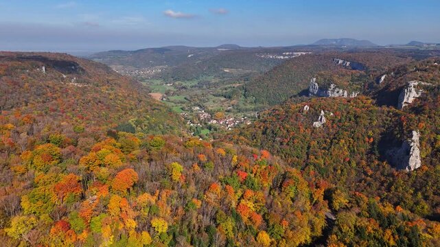 Drone pulls back above autumn forest revealing Sixt‑Fer‑&agrave;‑Cheval alpine village nestled in the Giffre valley, surrounded by steep limestone cliffs and Cirque du Fer‑&agrave;‑Cheval in the French Alps