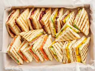 A variety of grilled sandwiches cut into triangles are displayed in a parchment lined tray