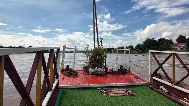 A vibrant Mekong river deck in Laos features plants, ropes, sandals, and a bright red platform.