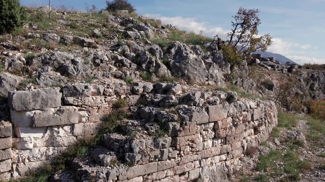 Close-up of Daorson&rsquo;s curved Illyrian stone wall and stairs set against a rugged hillside, showing weathered blocks, rocky terrain, surrounding the ancient archaeological site near Stolac.