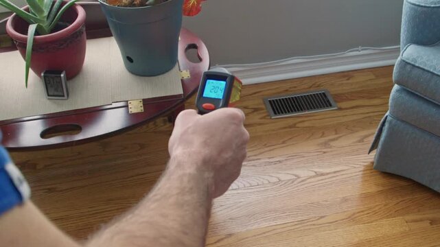 Home inspector uses a infra red thermometer to check the temperature coming out of floor register. Various temperatures are displayed.