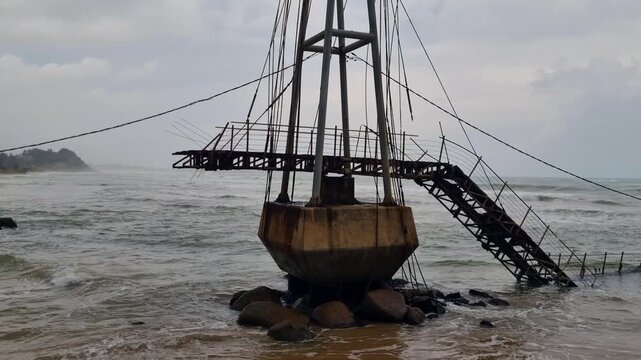 Shot of the old Paravi Duwa bridge remains in Matara, Sri Lanka, showing its weathered concrete base and rusted metal parts under an overcast sky on a stormy monsoon day