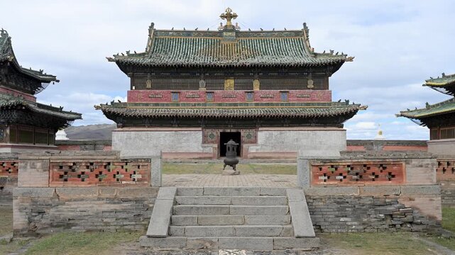 A quiet moment at Erdene Zuu Monastery, Mongolia. A man rests on a bench beneath a historic temple gate, framed by ancient red walls and ornate Buddhist roof details.