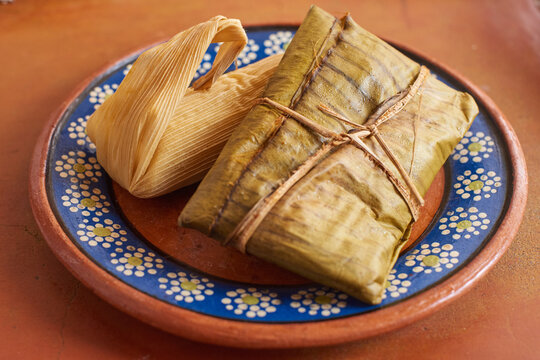 Tamal de hoja de pl&aacute;tano y tamal de hoja de ma&iacute;z sobre plato de barro tradicional del estado de Morelos, M&eacute;xico con luz contrastante.