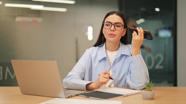 Focused professional listens to voice message, writing notes diligently. Shows concentrated individual managing tasks efficiently in modern office setting. Represents productive, attentive work.