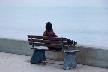 A woman is sitting on a bench by the sea, watching the sea