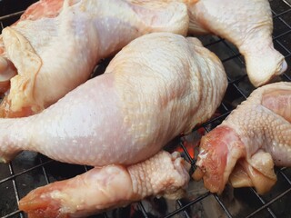 Grilling raw chicken legs over charcoal.
