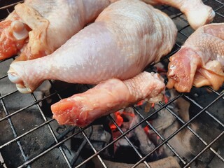 Grilling raw chicken legs over charcoal.