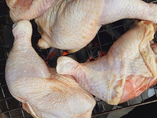 Grilling raw chicken legs over charcoal.