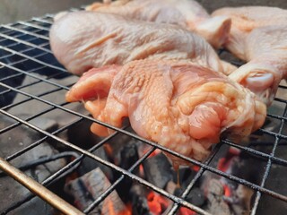 Grilling raw chicken legs over charcoal.