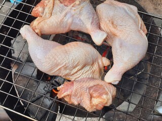 Grilling raw chicken legs over charcoal.