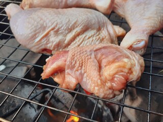 Grilling raw chicken legs over charcoal.