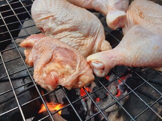 Grilling raw chicken legs over charcoal.
