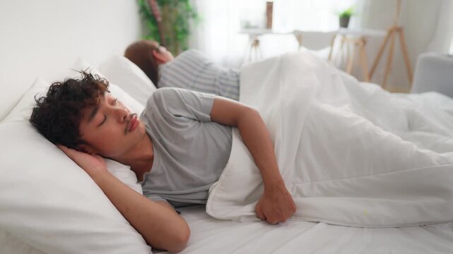 Asian LGBTQ couple lying down on bed with painful after fight argument.