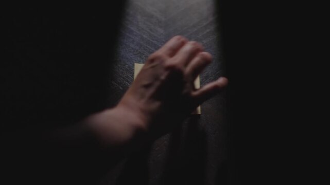 Slow motion close up footage of a hand writing out "Today" on a paper note, underlining it, and placing it on a table. Shot in dramatic lighting for an impressive title or transition.