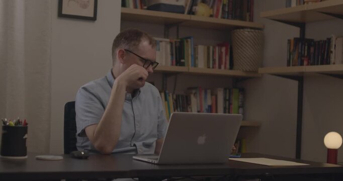 A man in glasses uses a calculator and computer to calculate numbers and do math in his office.