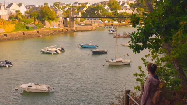 Le Bono village waterfront in Brittany, featuring traditional white houses, lush green and autumn-colored foliage, and small boats anchored on the calm Auray River.