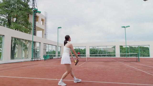 Asian sportsman and woman playing tennis match on outdoor clay court