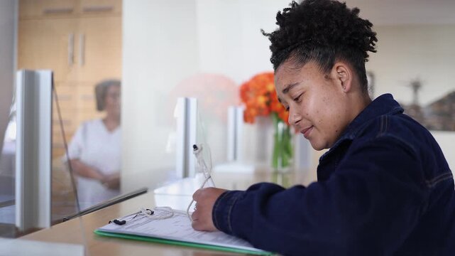 Young black woman fills out form at dental office reception counter